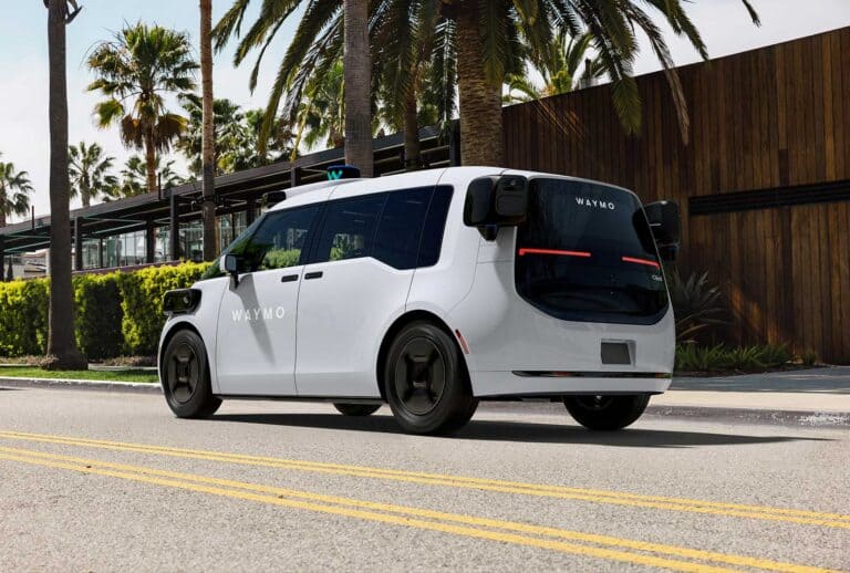 Autonomous Waymo vehicle driving on a city street with palm trees in the background.